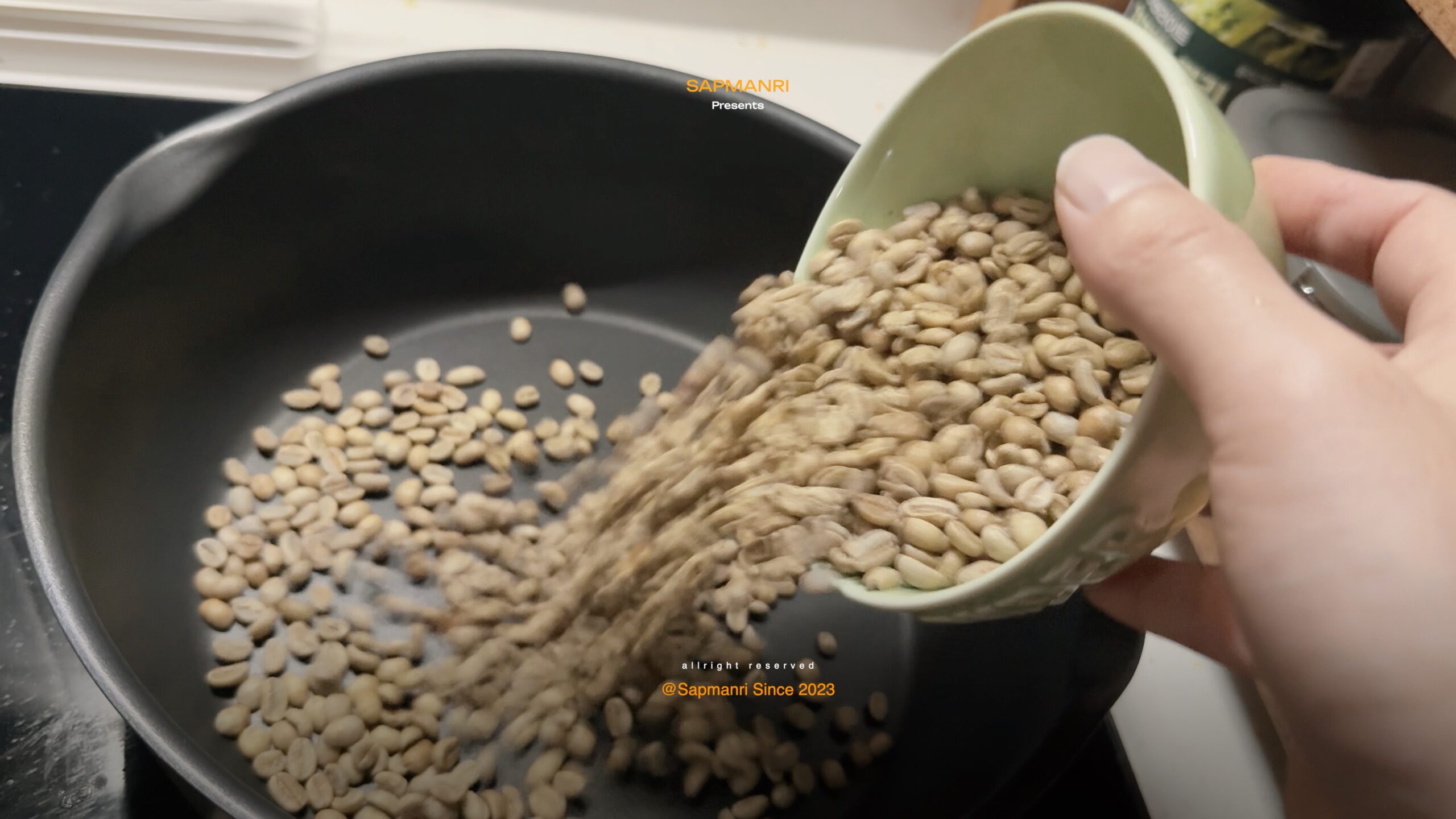 Green coffee beans being tipped into a cold frying pan.