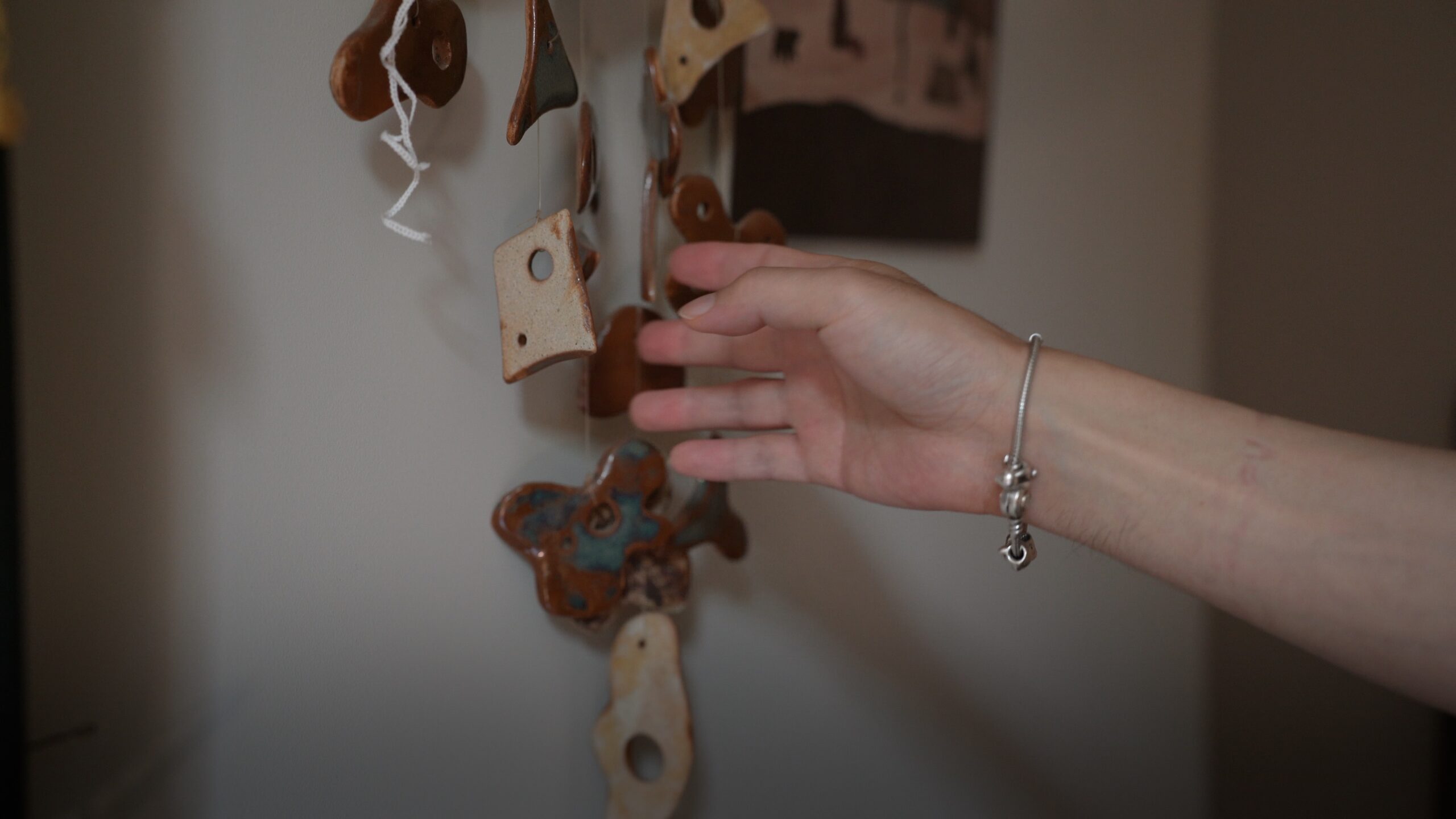 A hand touching a small group of hanging wooden and ceramic ornaments indoors.