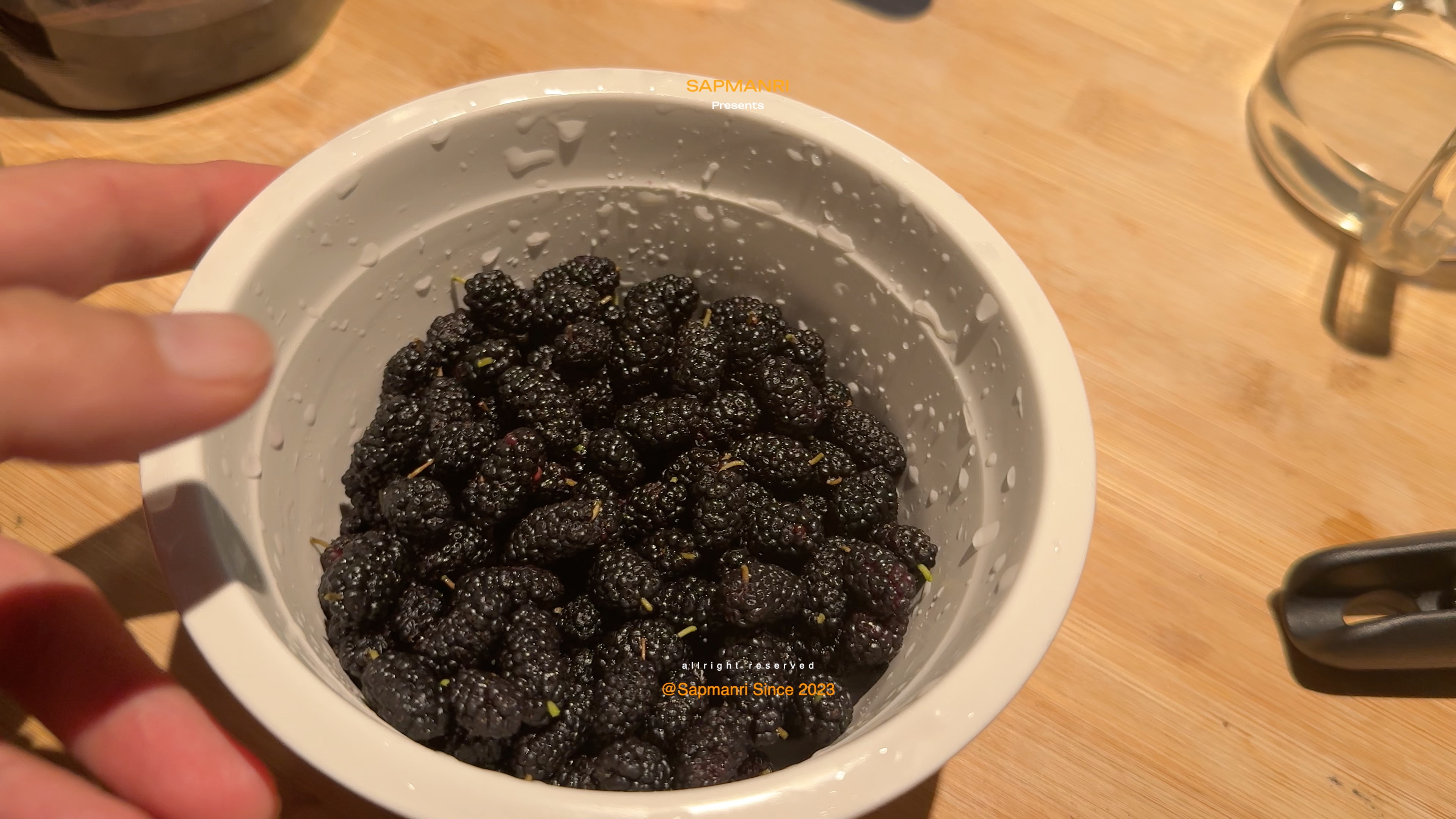A bowl filled with freshly picked black mulberries held over a kitchen counter.