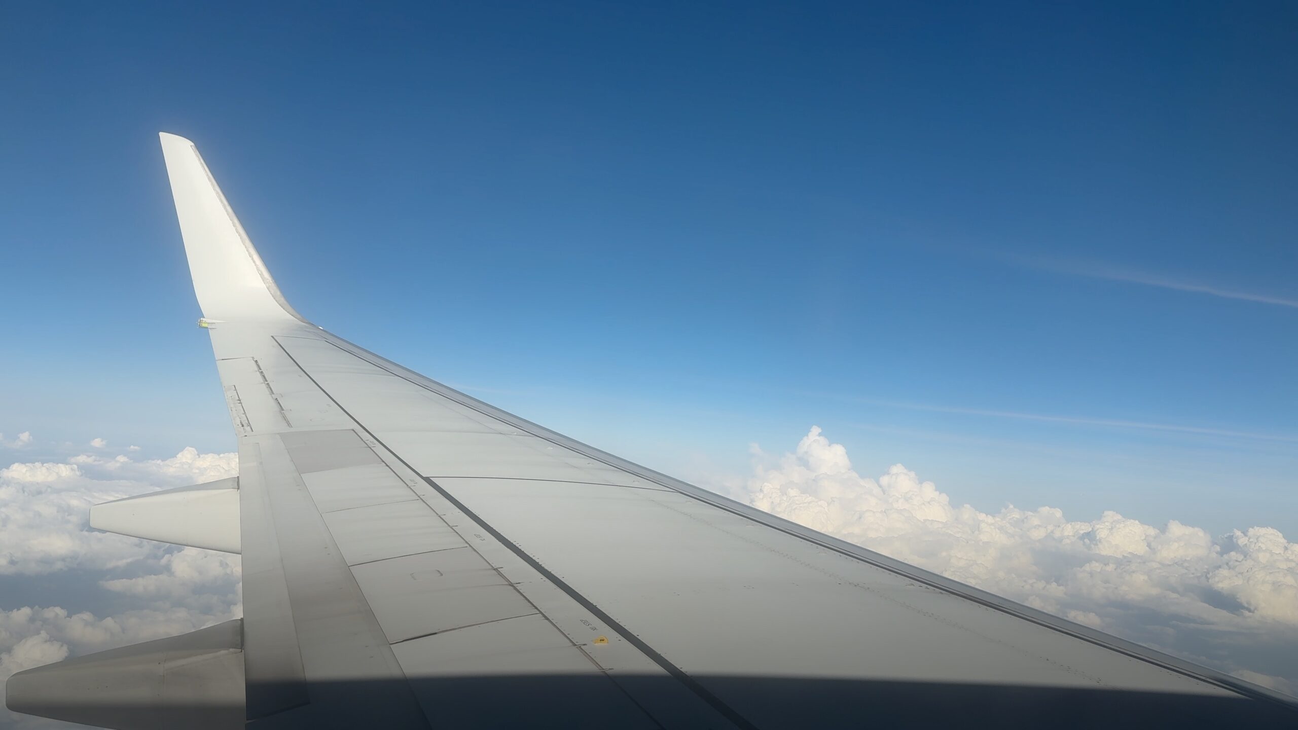 An aeroplane wing above white clouds under a deep blue sky.