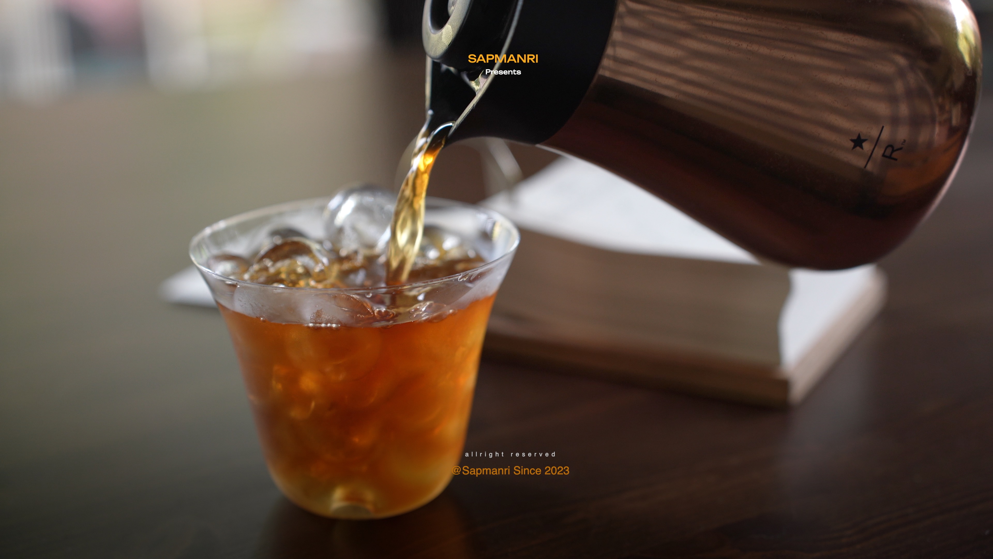 An amber iced drink being poured from a clear glass carafe into a tumbler.
