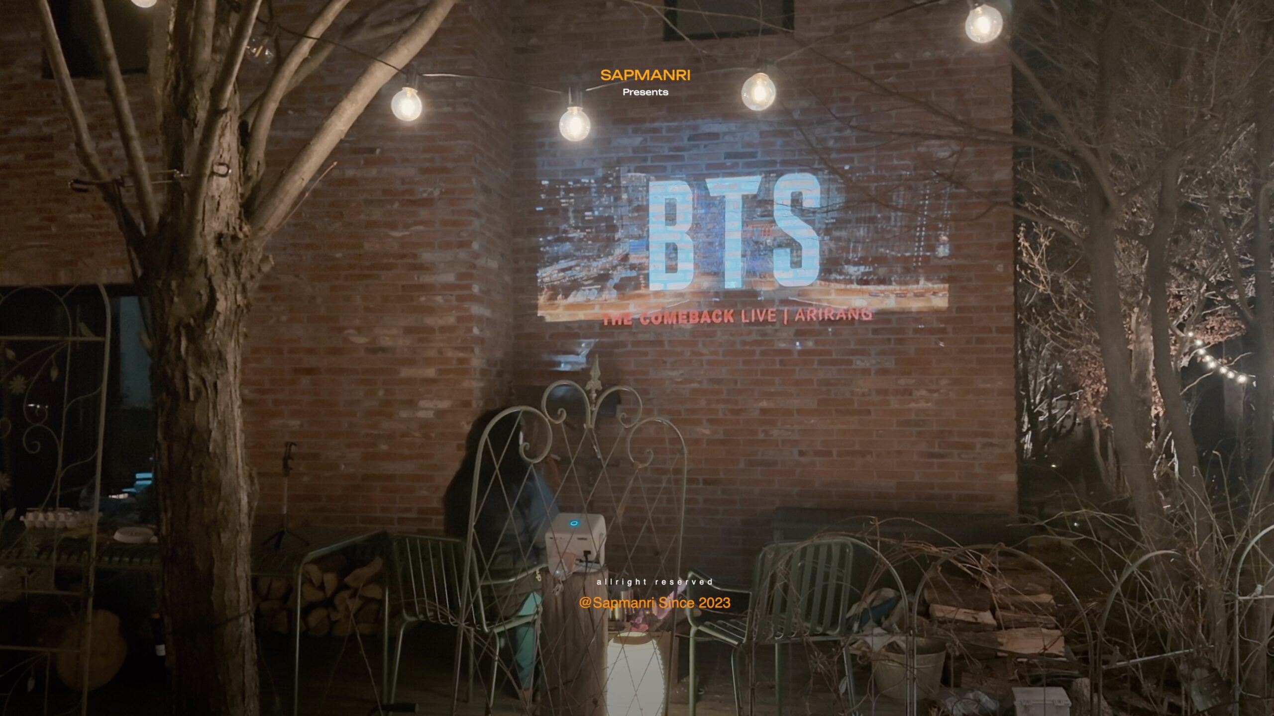 A BTS concert recording projected onto a brick wall in a dark backyard.