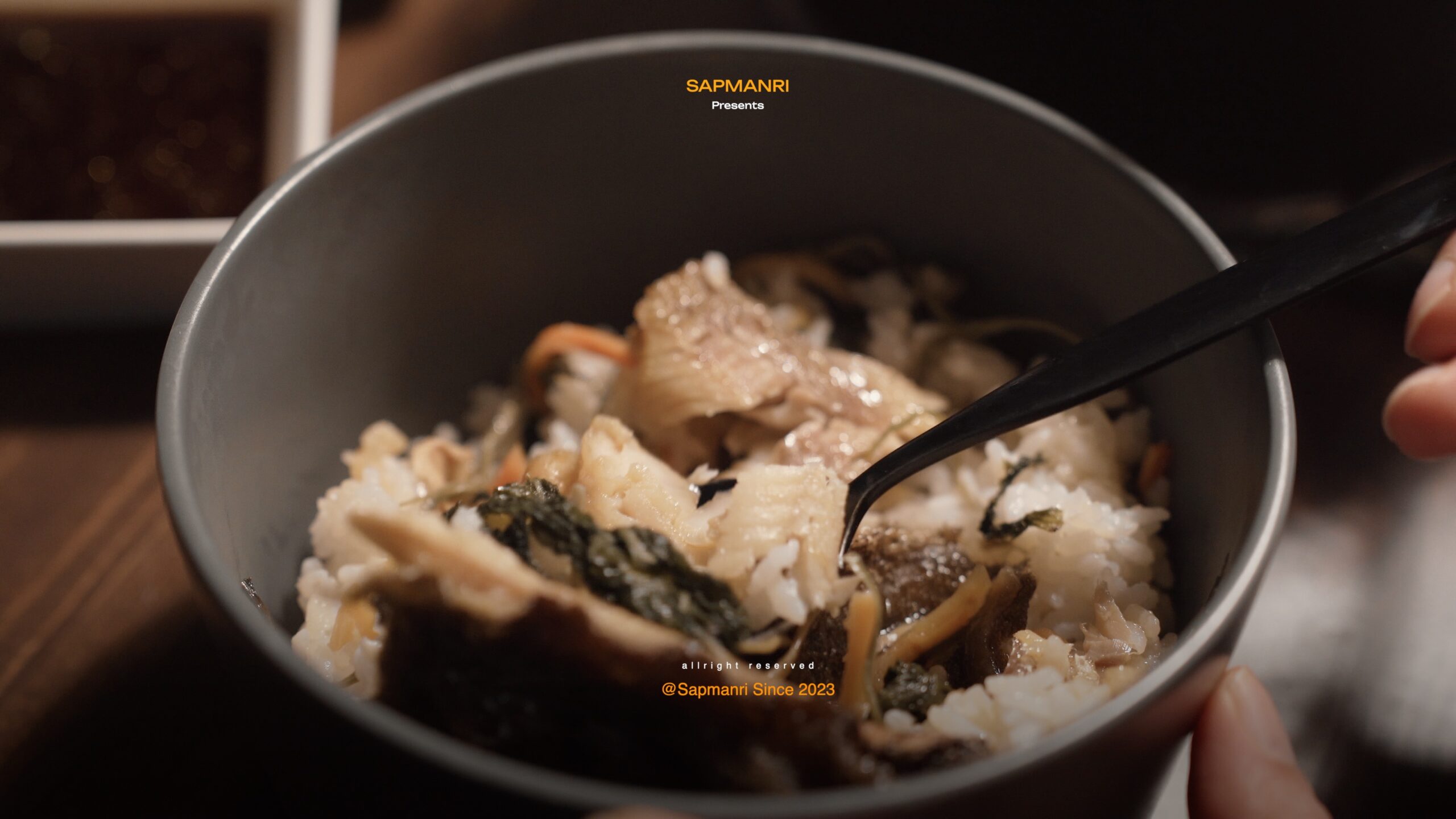 A bowl of mixed gondre rice with pieces of cooked fish being eaten with a black spoon.