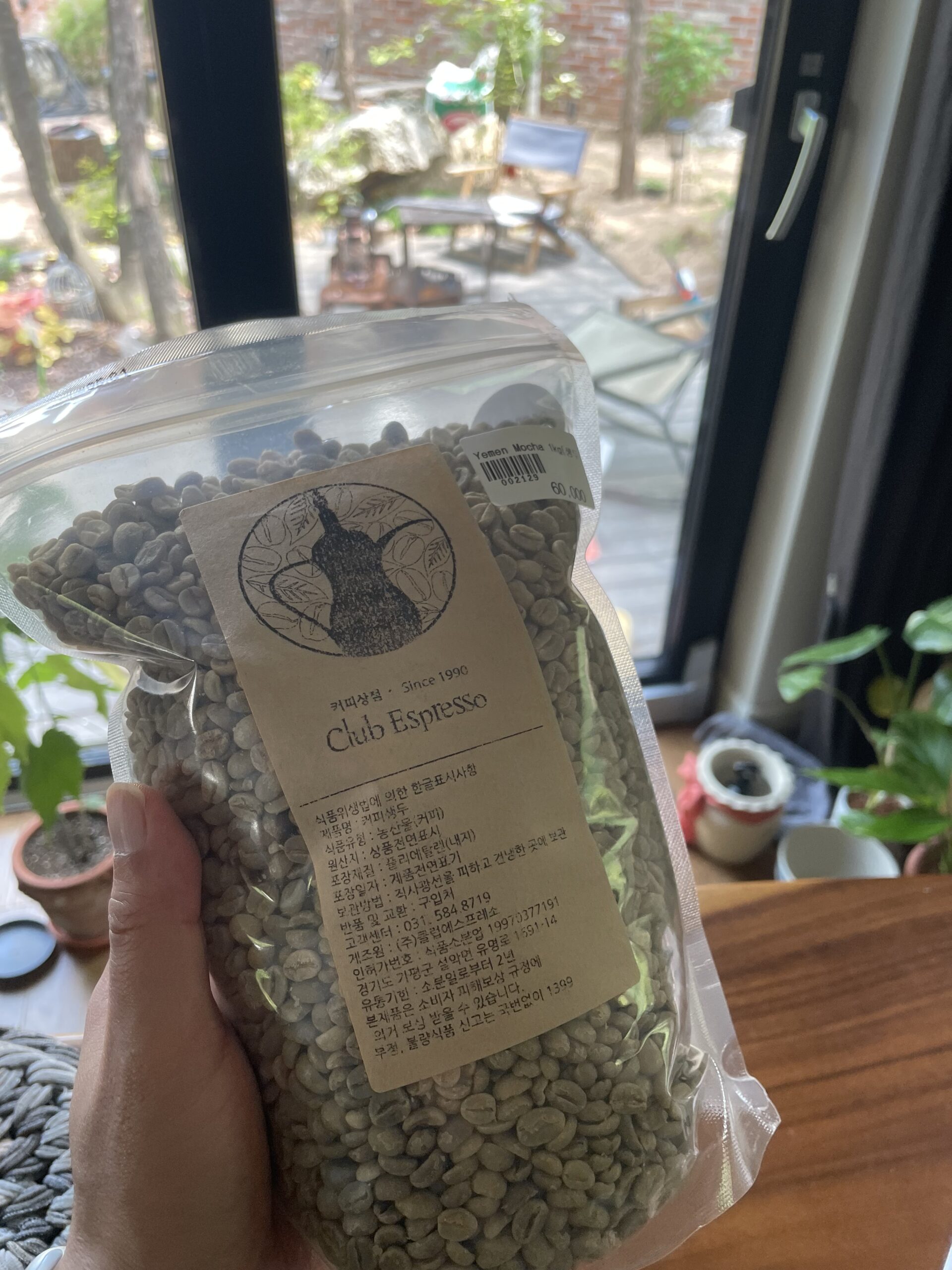 A hand holding a sealed bag of green Yemen Mocha coffee beans.