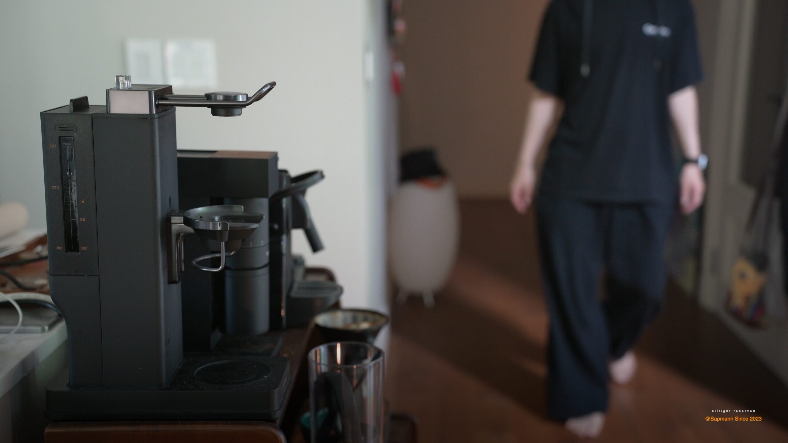 A person preparing a drink beside a compact coffee machine on a home counter.