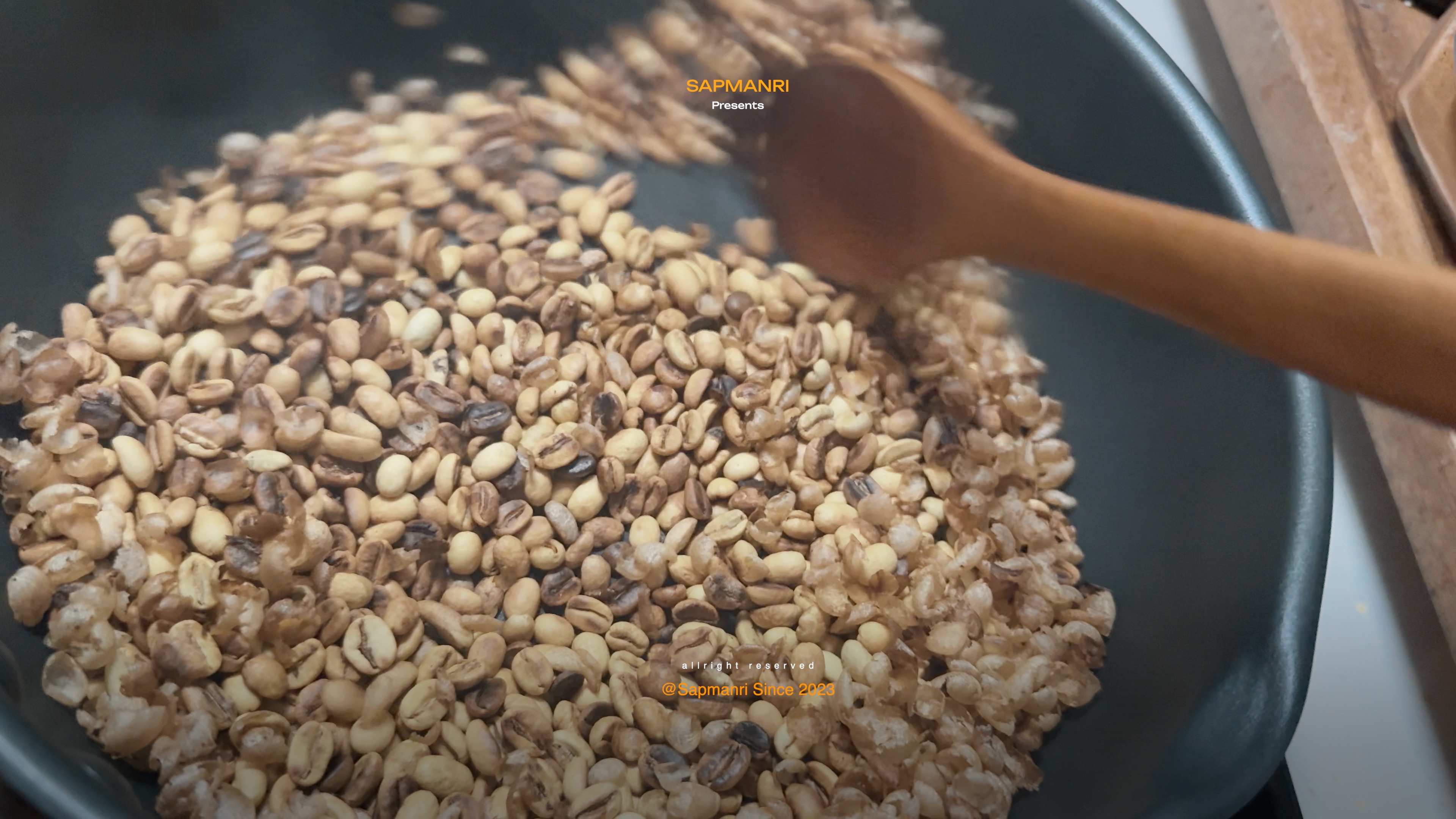 A pan holding coffee beans roasted to visibly different shades, mixed with loose papery chaff.