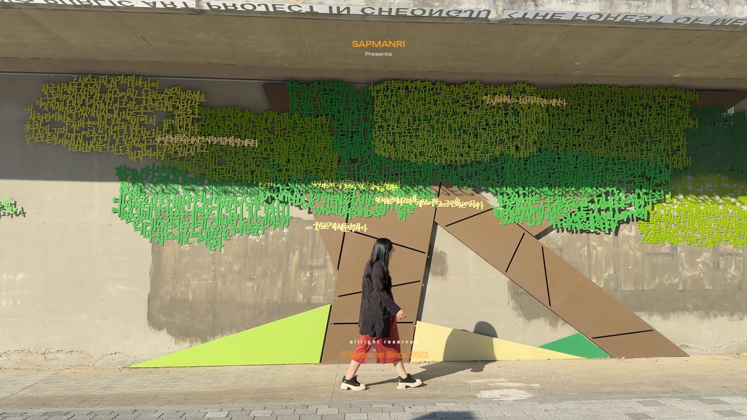A person walking past a large green-and-brown text mural at Cheongju's Dongbu Warehouse.