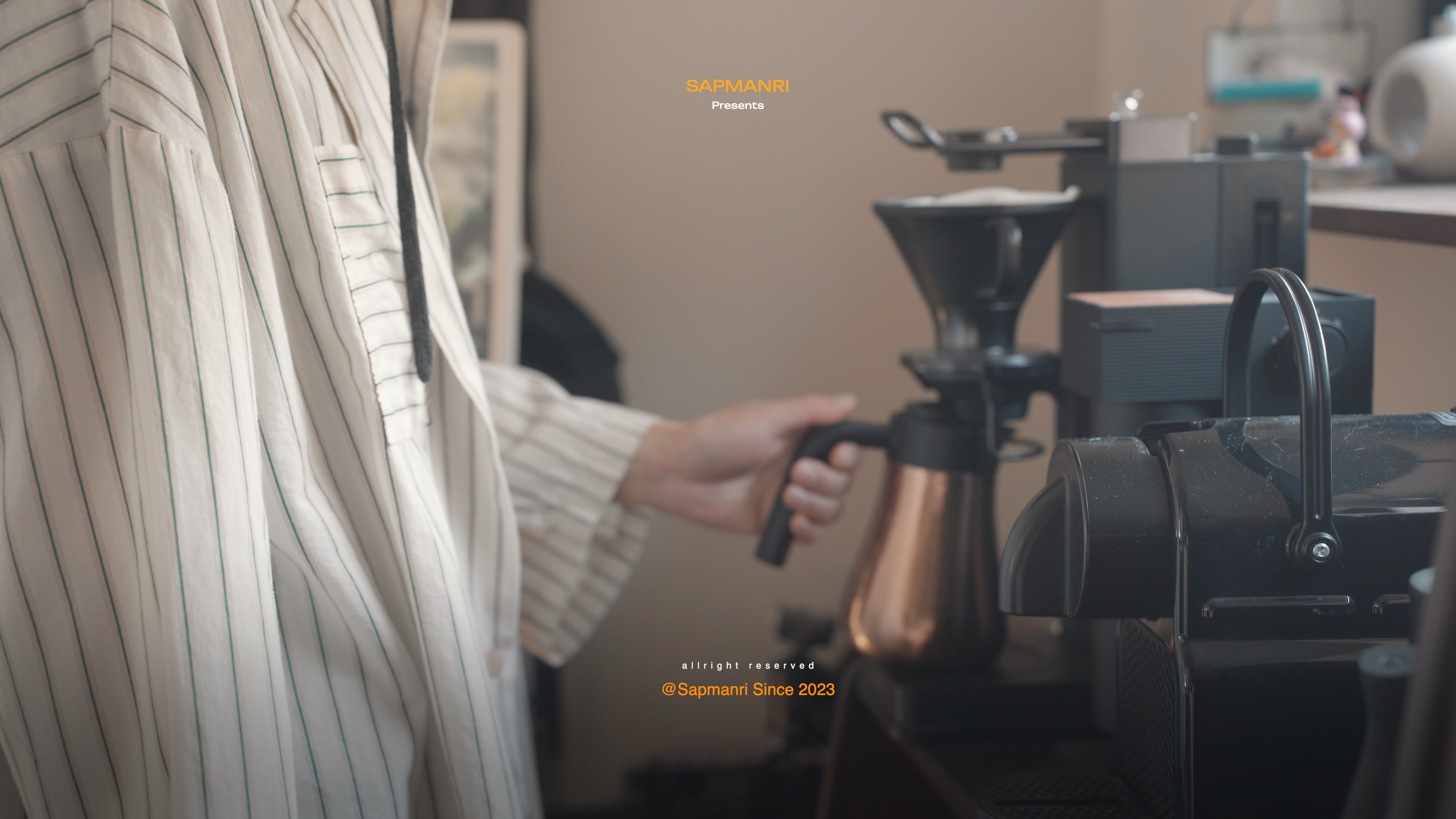 A cafe worker holding a portafilter beside espresso grinders and a black coffee machine.