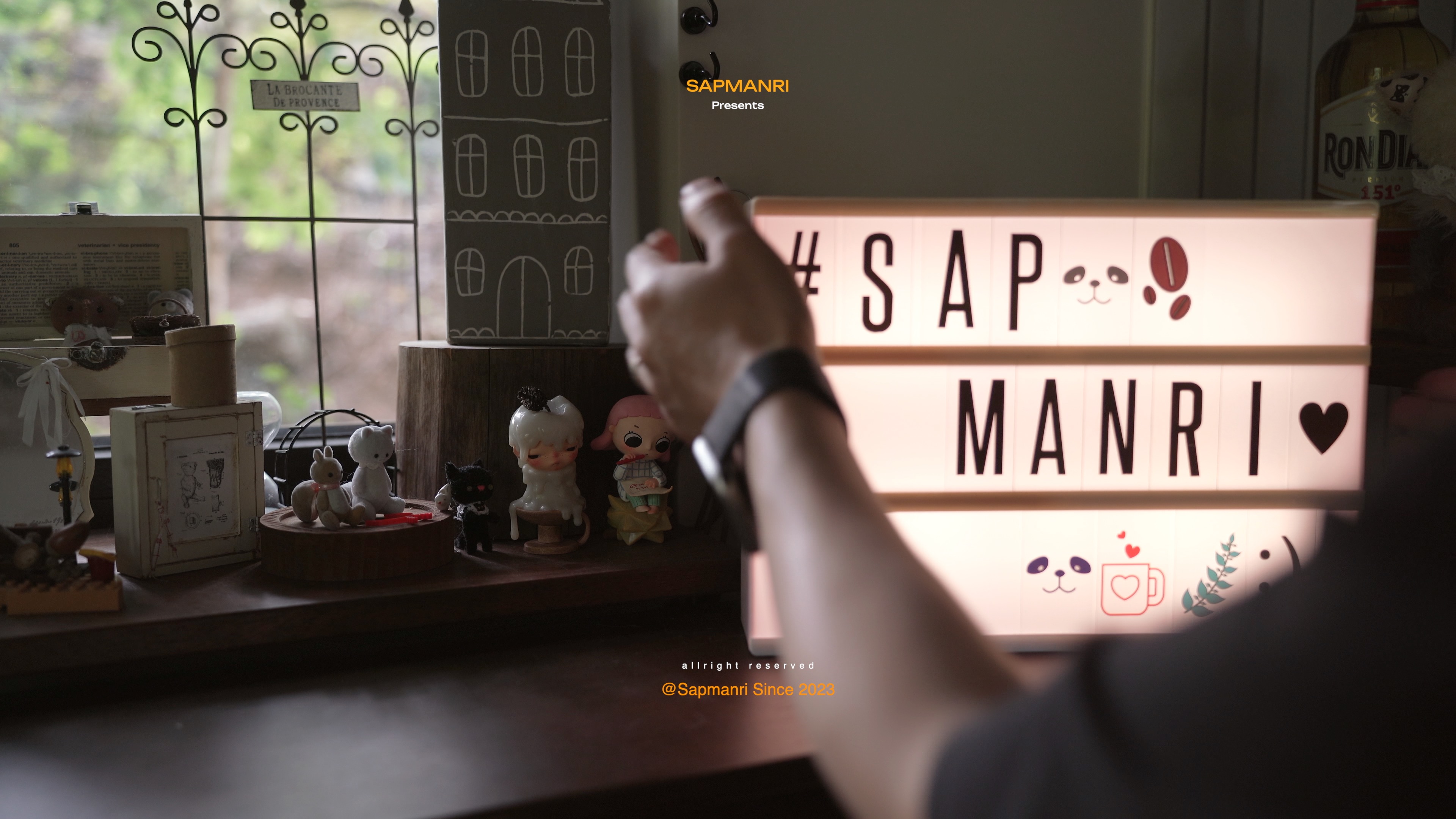 A hand switching on a glowing SAP MANRI lightbox among small objects on a shelf.