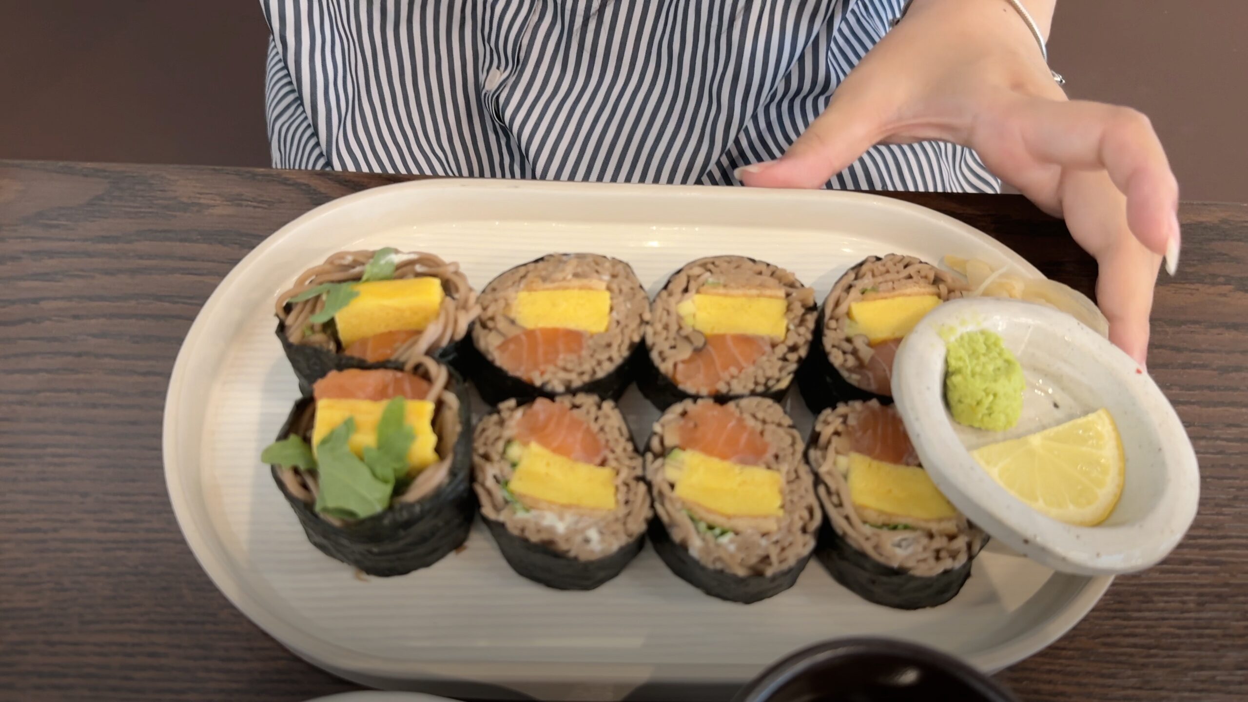 A plate of sliced gimbap presented on a table, with lemon and wasabi at the side.