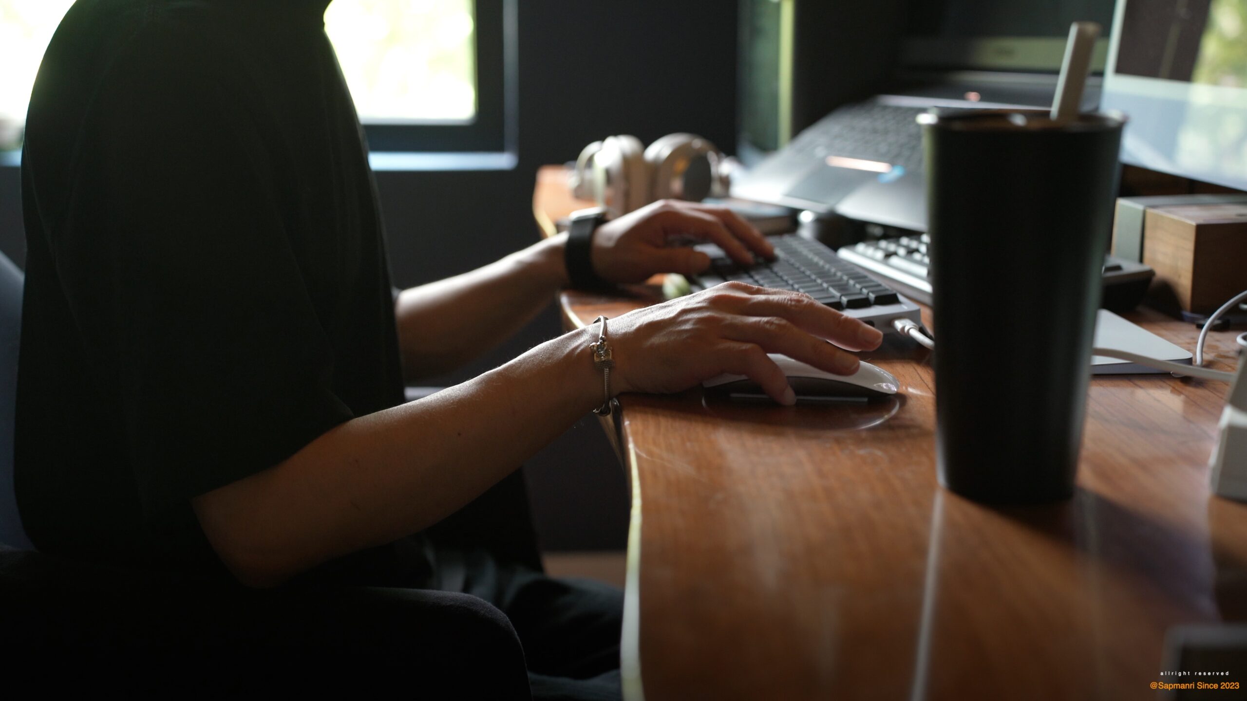 A person seated at a desk, editing work on a large monitor in a home studio.
